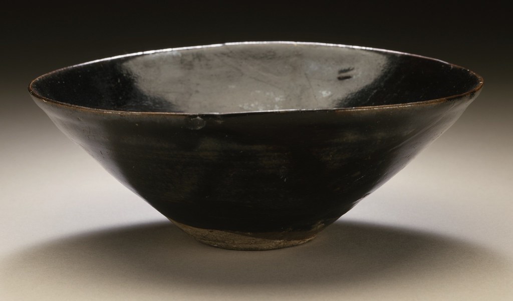 A conical tea bowl with a glossy black glaze and an unglazed foot