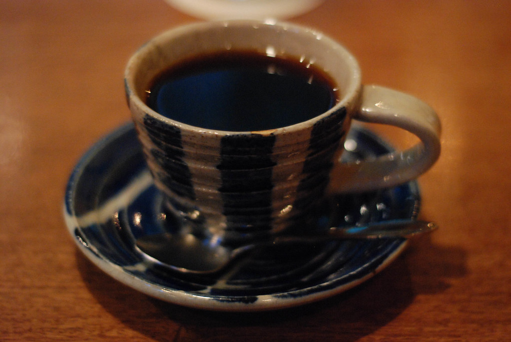 A thrown stoneware cup with blue-black vertical stripes on a matching saucer, filled with coffee