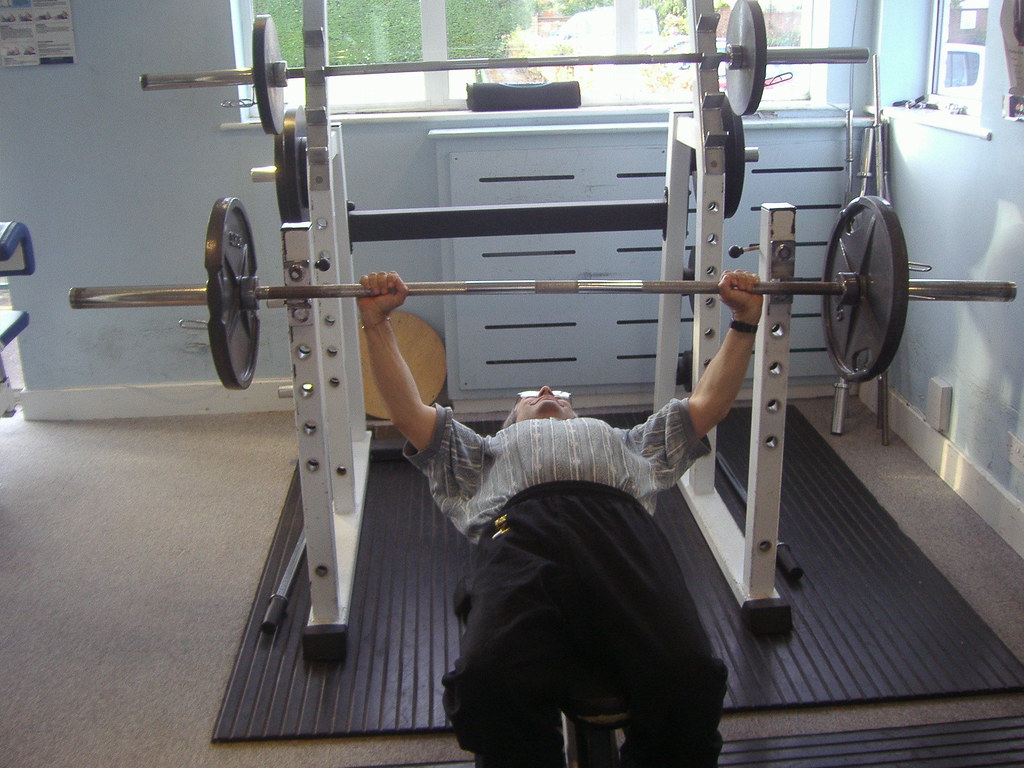 A lifter pressing a barbell in a small training room