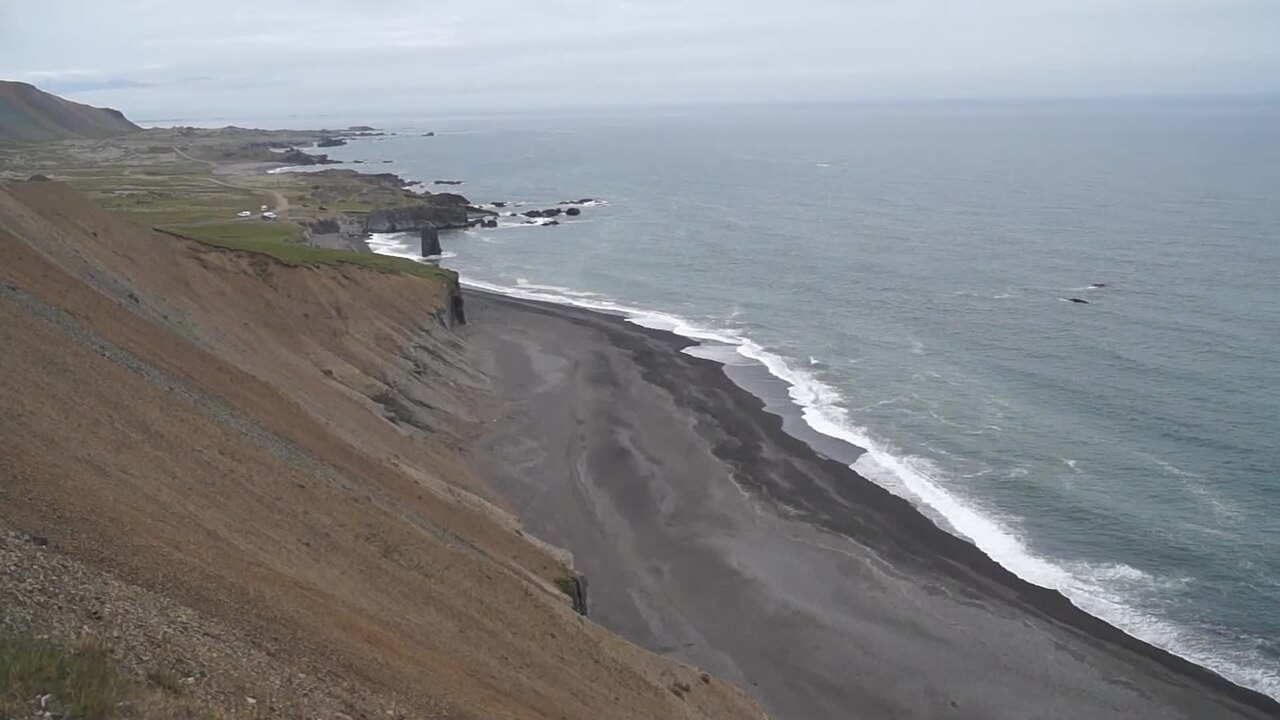 Cliffs running down to a long black-sand beach, with surf along the shoreline
