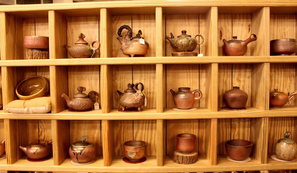 Wooden shelving holding rows of handmade teapots, cups and bowls in brown and green glazes